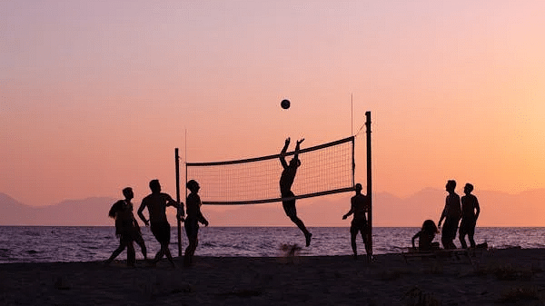 Silhouettes of people playing volleyball on a beach at sunset, with the net and ball visible.