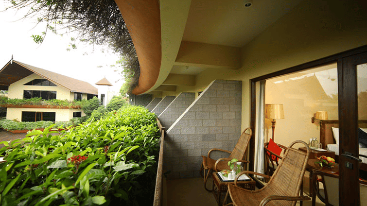 The balcony of the Ixora Room at Uday Suites offering a view of lush greenery and a building