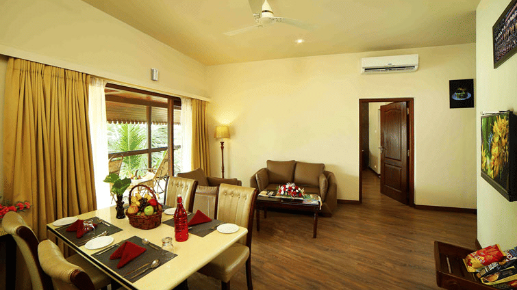 A well-lit hotel suite features a dining area with a set table, a lounge area with a sofa, and a doorway leading to another room at UDS Group of Hotels.