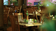 The dimly lit, empty tables and wooden chairs in what appears to be a restaurant at Grasshopper reataurant Uday Samudra Leisure Beach Hotel.