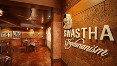 Entrance to Swastha Vegetarianism restaurant featuring a warmly lit interior, wooden furniture, and decorative walls with the restaurant's name displayed at Uday Samudra Leisure Beach Hotel, Kovalam