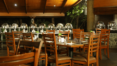 Southern Express at Uday Suites featuring a dimly lit indoor dining area with multiple buffet stations with covered dishes and several empty wooden tables and chairs