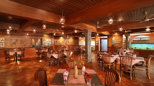 Spacious dining area of Swastha Vegetarianism restaurant featuring wooden decor, neatly arranged tables with napkins, and warm ambient lighting at Uday Samudra Leisure Beach Hotel, Kovalam