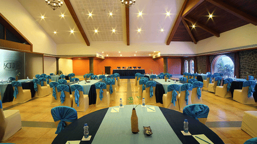 A spacious Vizhinjam Hall at Uday Samudra Leisure Beach Hotel, Kovalam, is prepared for an event with round tables and blue-draped chairs.
