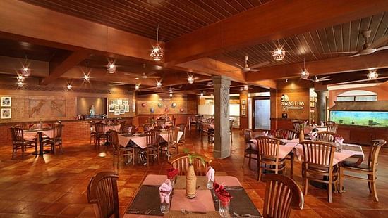 Spacious dining area of Swastha Vegetarianism restaurant featuring wooden decor, neatly arranged tables with napkins, and warm ambient lighting at Uday Samudra Leisure Beach Hotel, Kovalam