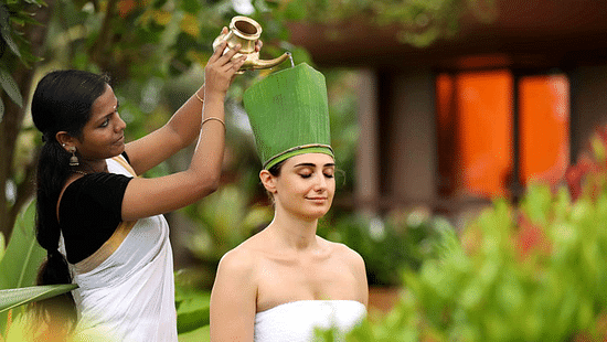A woman sitting outdoor receiving a kind of therapy with her eyes closed at Ayurveda Spa, Uday Backwater Resort