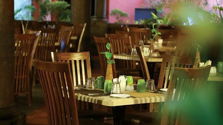 The dimly lit, empty tables and wooden chairs in what appears to be a restaurant at Grasshopper reataurant Uday Samudra Leisure Beach Hotel.