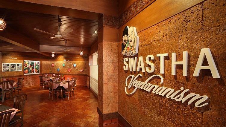 Entrance to Swastha Vegetarianism restaurant featuring a warmly lit interior, wooden furniture, and decorative walls with the restaurant's name displayed at Uday Samudra Leisure Beach Hotel, Kovalam