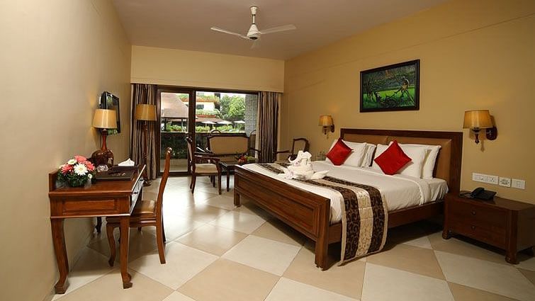 Mystica Room at Uday Suites showcases a plush bed, a desk, and a balcony with chairs and a ceiling fan, all under warm lighting