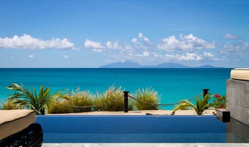  A luxurious infinity pool seamlessly blends with the turquoise ocean under a blue sky - Tamarind Hills Resort and Villas - Antigua