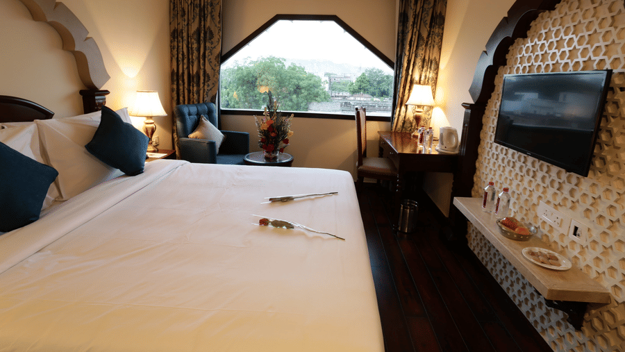 A bedroom at Comfort Inn Sapphire by Eastlynn Collections, Jaipur with queen size bed, window, armchair,, work desk, and wall-mounted TV inside the room.