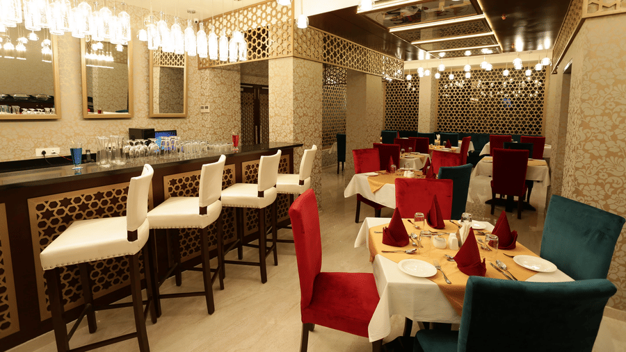 A dining area at Comfort Inn Sapphire by Eastlynn Collections, Jaipur with tables, chairs, bar counter, and hanging lights.