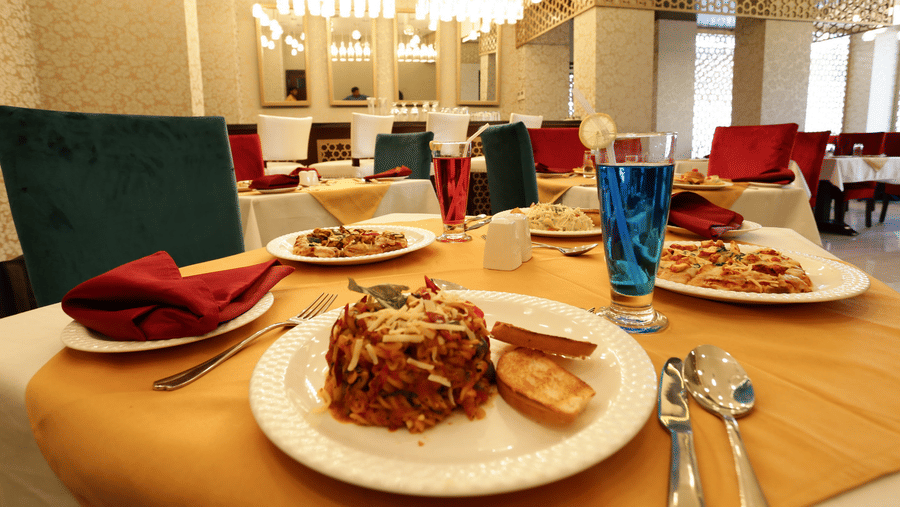 A dining setup at Comfort Inn Sapphire by Eastlynn Collections, Jaipur with plated food, glasses, cutlery, and table arrangement.