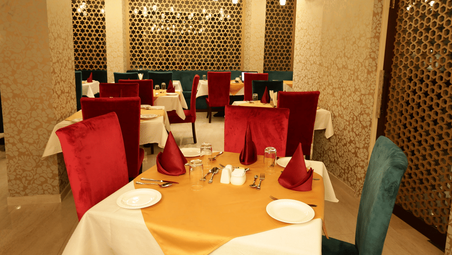 A dining area at Comfort Inn Sapphire by Eastlynn Collections, Jaipur with tables, chairs, table settings, and patterned wall panels.
