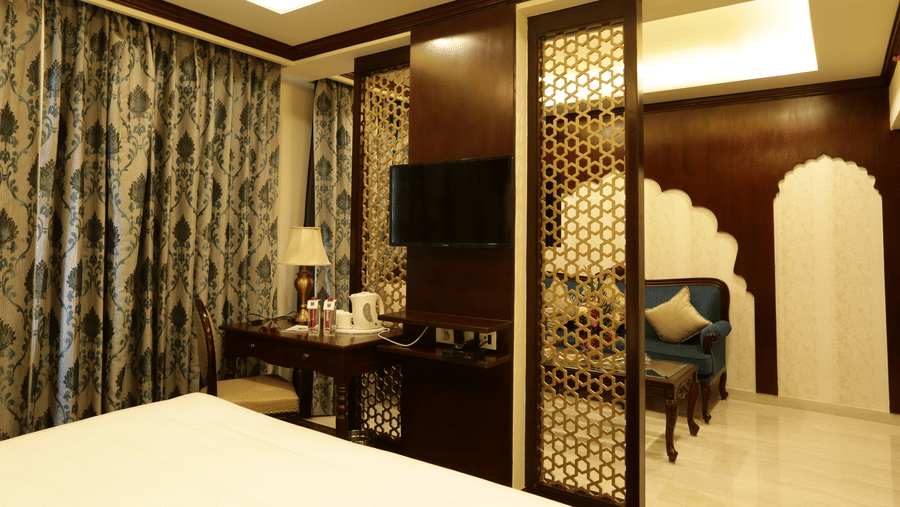 A bedroom at Comfort Inn Sapphire by Eastlynn Collections, Jaipur with king size bed  bed, wall-mounted TV, partition panel, curtains, and seating area.