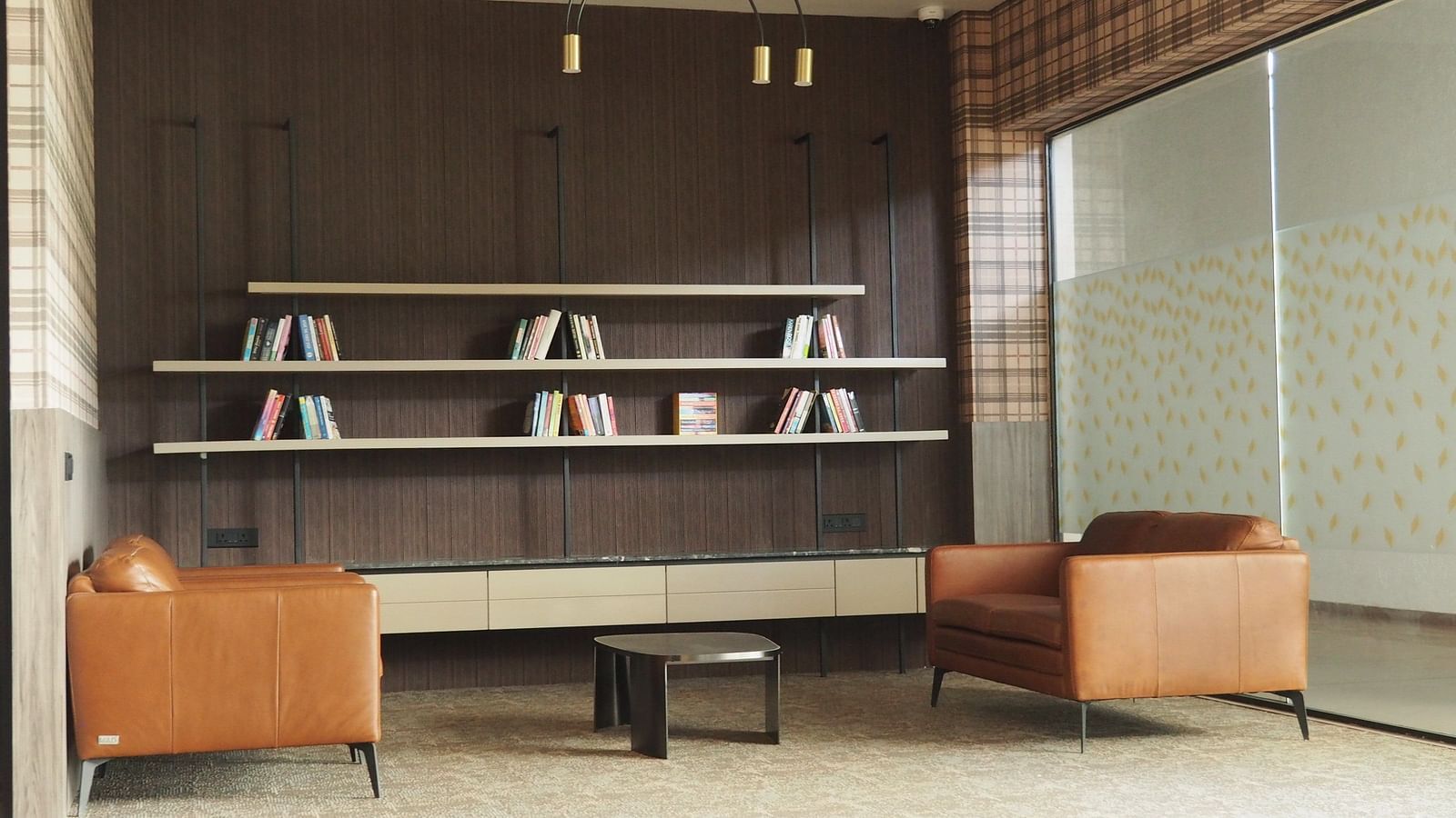 A lounge area with armchairs and shelves, separated by a glass partition - Club Charholi, Pune 