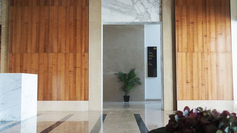 A hallway with wooden panelled walls and a plant, leading to a doorway - Club Charholi, Pune 