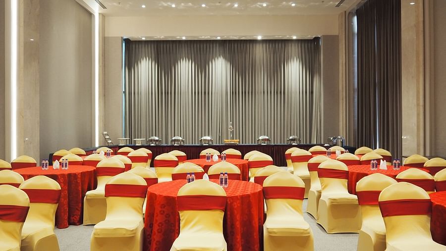 A conference hall with round tables and chairs, facing a curtained stage - Club Charholi, Pune 