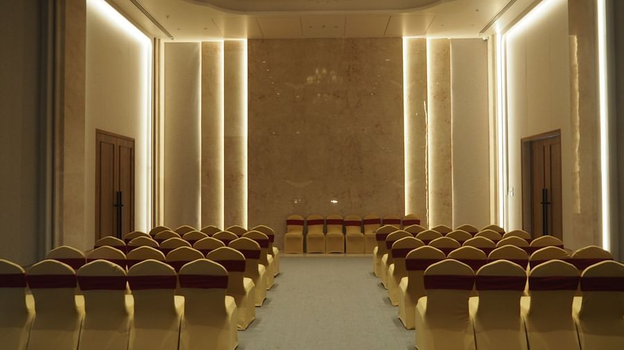 A grand hall with rows of chairs facing a stage, lit by a chandelier - Club Charholi, Pune 