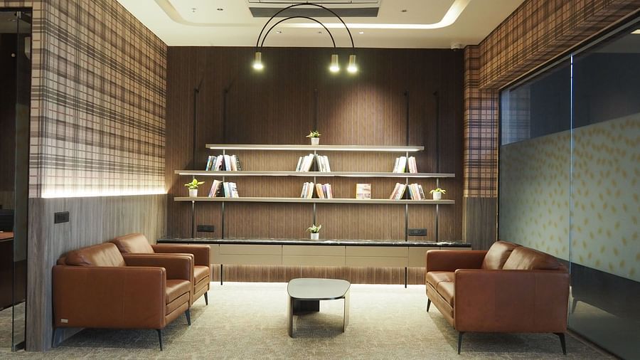 Two brown armchairs facing each other with a small table between them, under a bright ceiling light - Club Charholi, Pune 