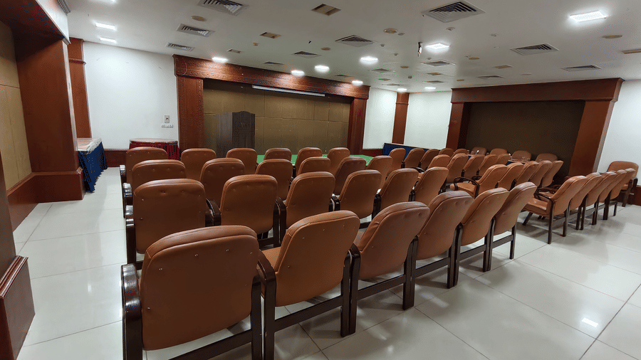 Rows of cushioned seats arranged in an auditorium setting facing a stage area, wooden podium, and wall panelling at DSF Grand Plaza, Tuticorin.