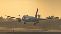 Airplane taking off or landing on runway during sunset, with sky glowing in the background.
