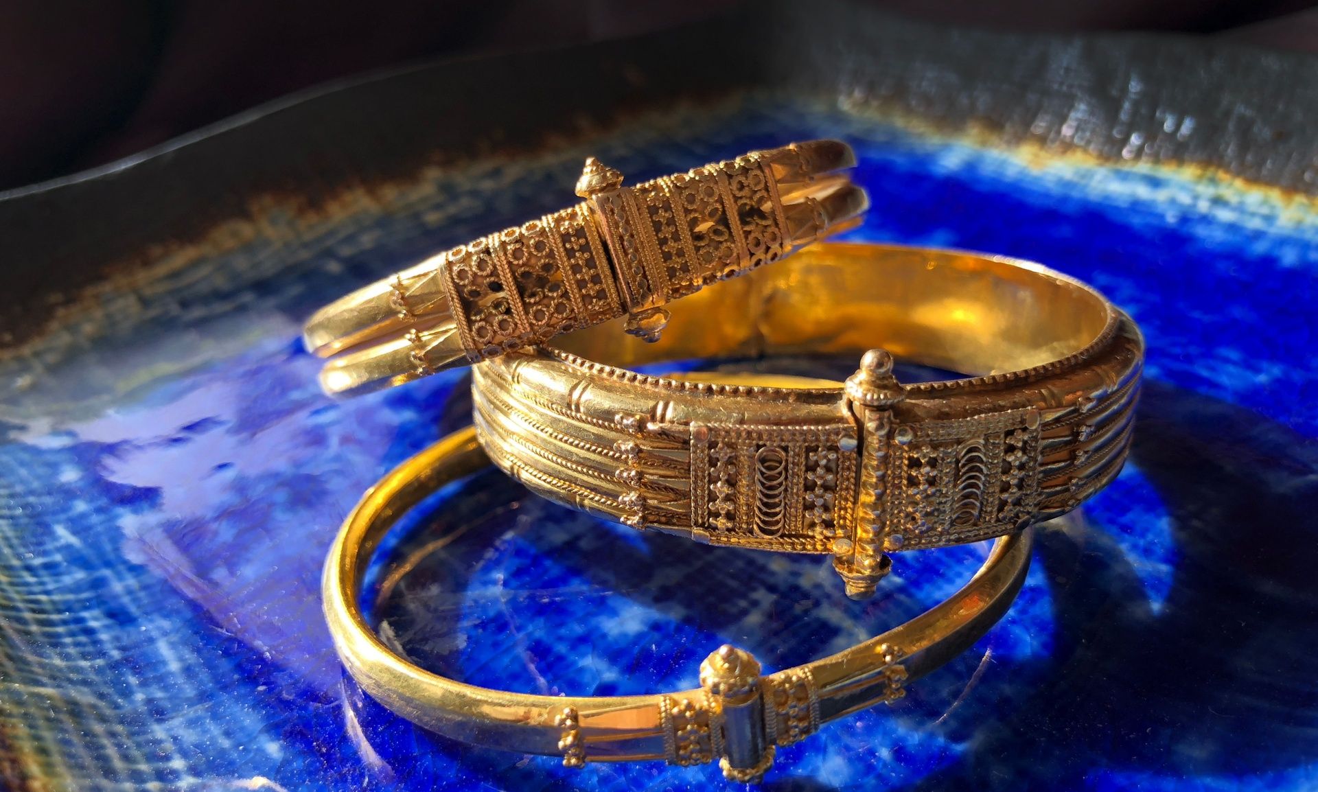 Three gold kadagas with intricate designs on blue.