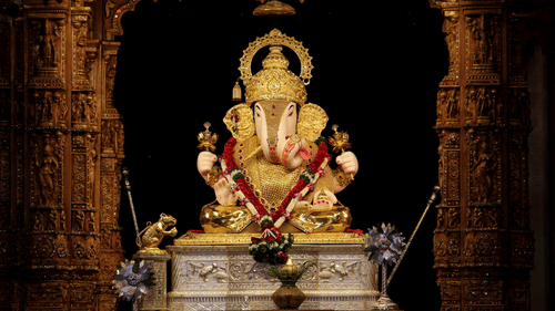 A beautifully decorated idol of Lord Ganesha during Ganesh Chaturthi in Chennai sitting inside a dimly lit temple shrine, surrounded by ornate pillars and traditional festive decor