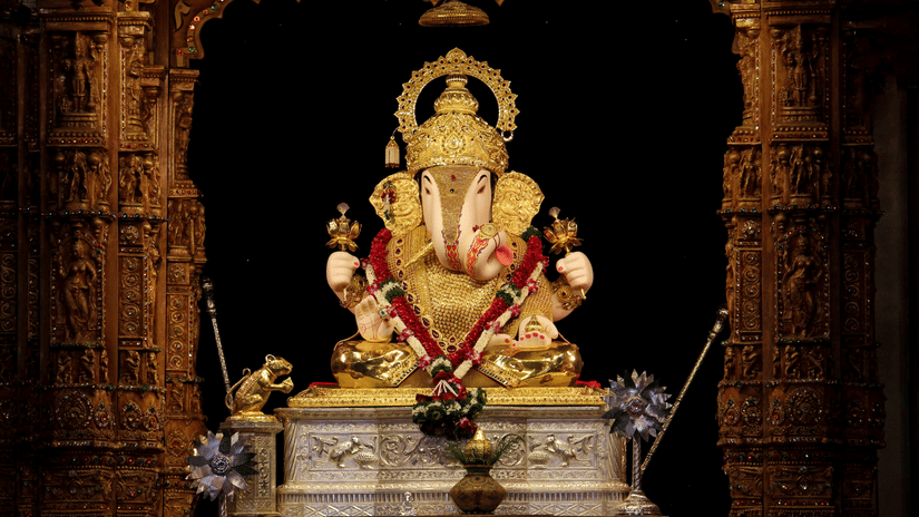 A beautifully decorated idol of Lord Ganesha during Ganesh Chaturthi in Chennai sitting inside a dimly lit temple shrine, surrounded by ornate pillars and traditional festive decor