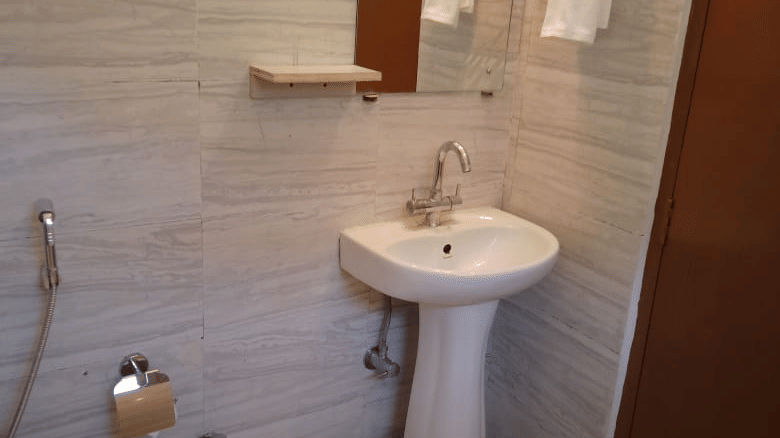 Compact bathroom with a pedestal washbasin, mirror, toilet and tiled walls.