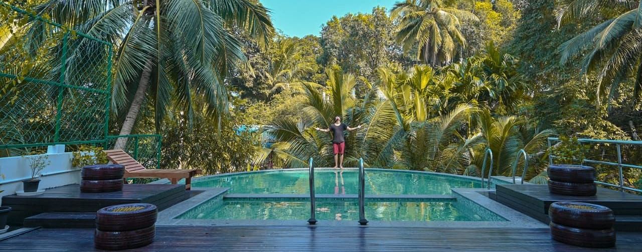 A serene outdoor swimming pool nestled amongst dense tropical foliage and palm trees under a clear blue sky - Sea Hills Hotels, Sri Vijaya Puram (Port Blair)