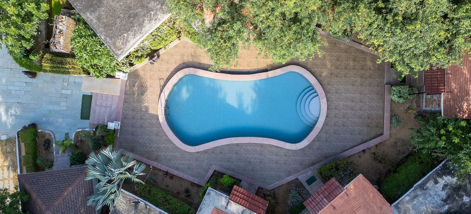 Aerial view of a swimming pool at Valley by Grassfield, nestled among lush trees and surrounded by accommodations.
