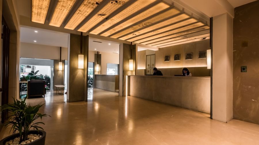  A spacious, contemporary hotel lobby featuring a long reception desk, warm lighting from ceiling beams, and a welcoming ambience at Shilton Dee Cee.