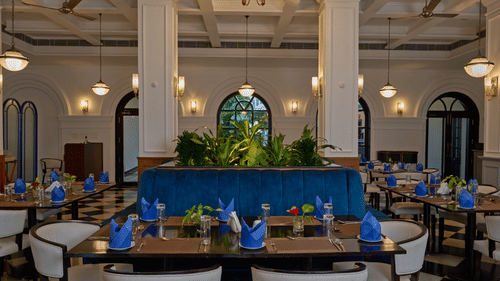 Elegant dining room at the best hotel in Fort Kochi, Old Court House by Abad, featuring a blue velvet booth, white columns, and set tables.