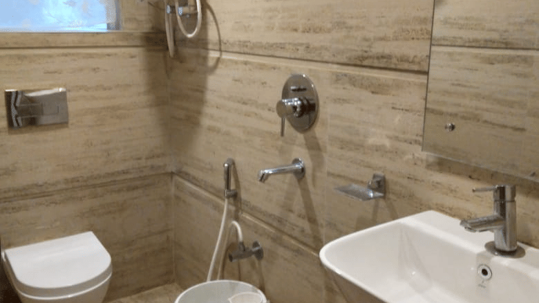 Modern bathroom with light beige tiled walls, a shower, toilet, sink, and a water heater mounted above at Hotel Dolphin Darjeeling.
