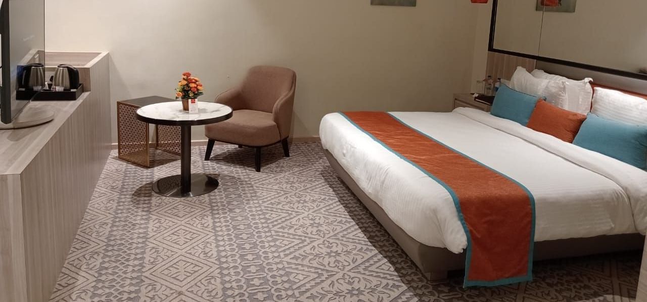 Modern hotel room with twin beds, a small table and chair, soft lighting, and minimalist decor.