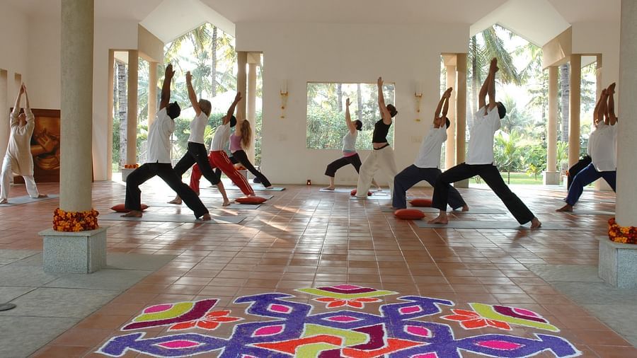 People doing yoga poses in a bright room, colorful rangoli on floor - Shreyas Retreat