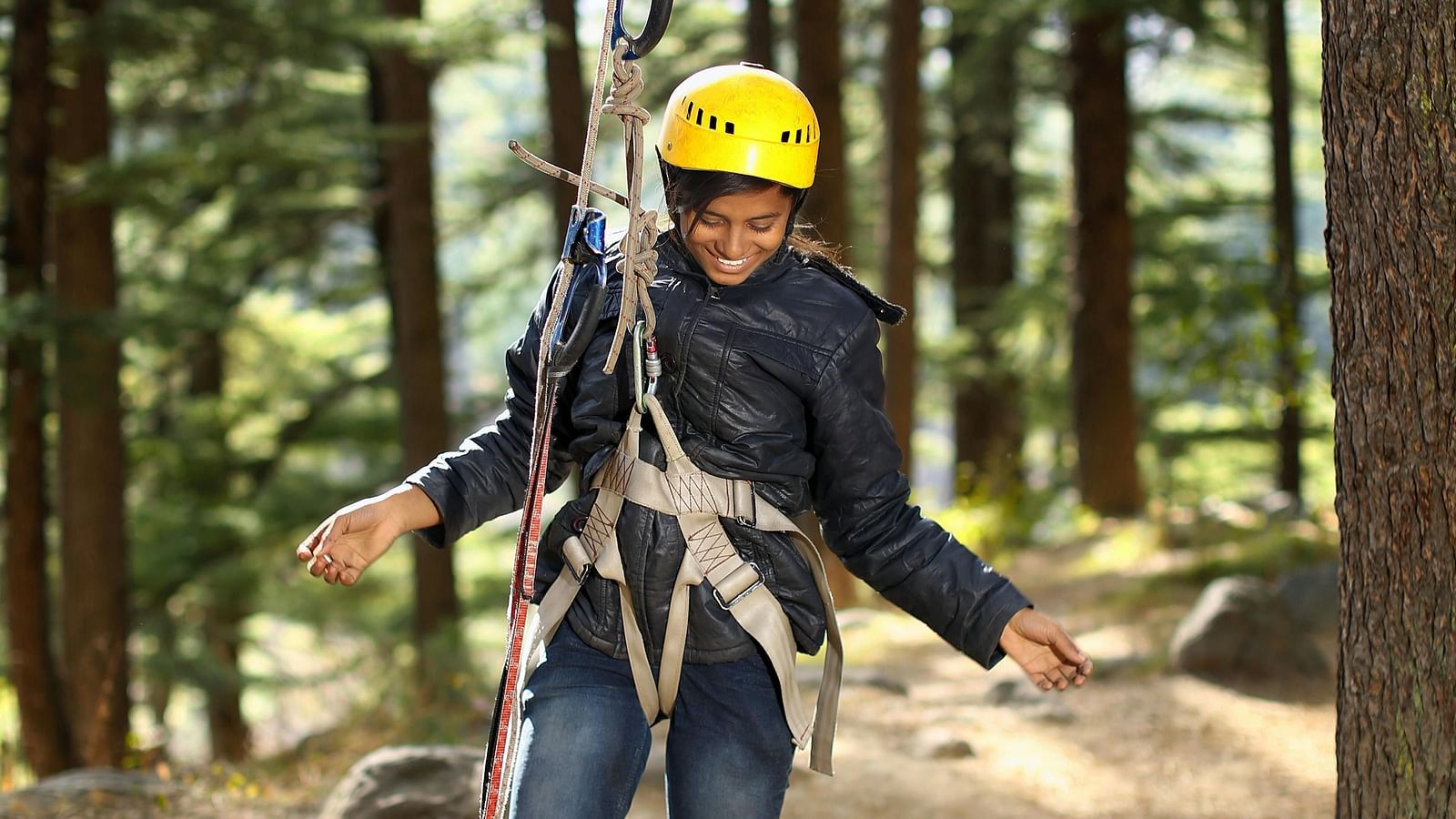 A close-up view of a woman hanging from a zipline rope, set against a backdrop of lush greenery in the forest.