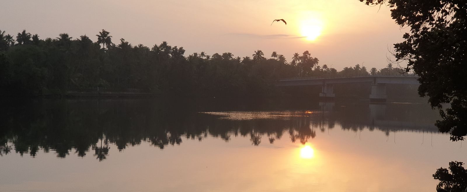 A tranquil landscape of a lake or river at sunset or sunrise, with reflections of the sky and trees on the water.