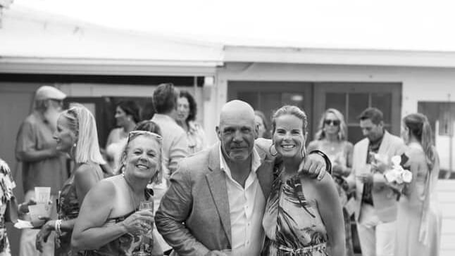 People stand on a covered terrace, some raising hands with drinks, with wedding attire, Abaco Inn.
