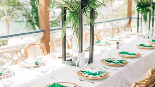 A corner view of a long table set with plates, glasses, and napkins under a wood canopy, Abaco Inn.