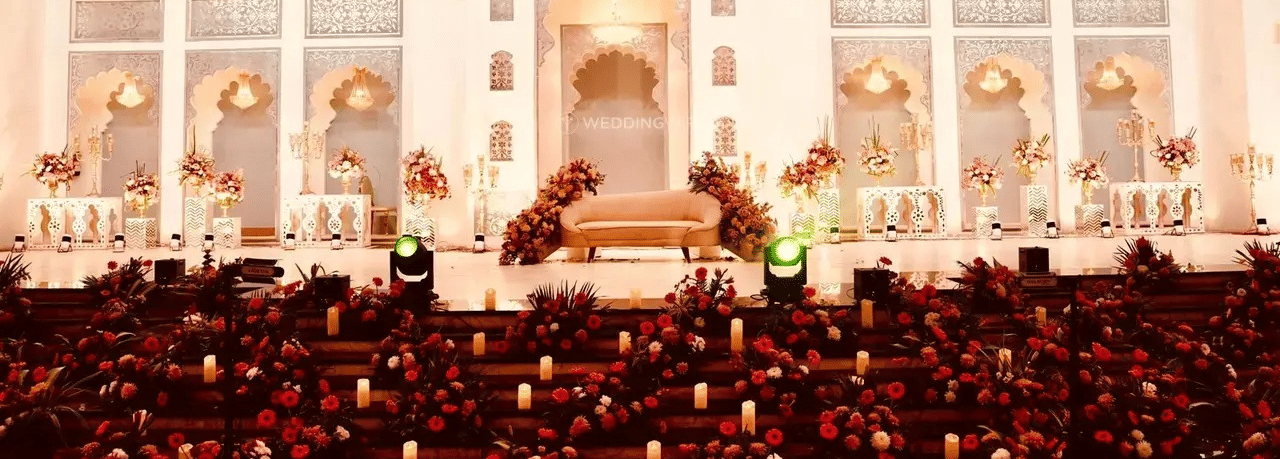 Indoor banquet hall with decorative stage, chandeliers and rows of chairs at Beelwa Palace, Jaipur