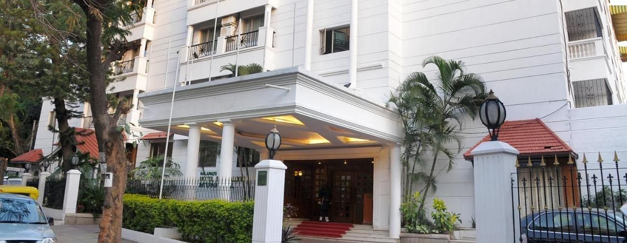Nalapad Hotel Bangalore International, a white building with a covered entrance, landscaping, and parking.