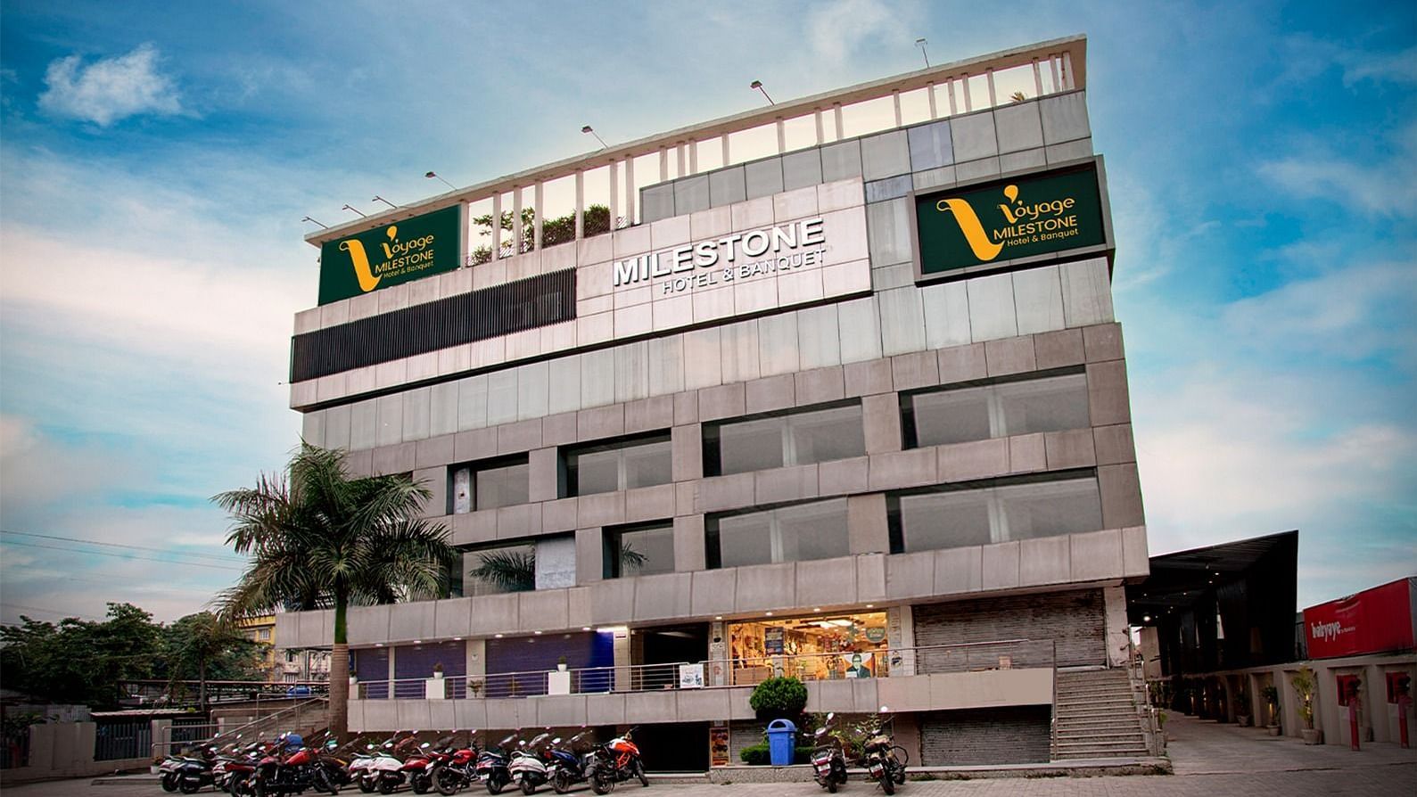 Voyage Milestone Hotel and Banquet is a modern glass and concrete building in Bengaluru, Karnataka, India, under a bright blue sky.