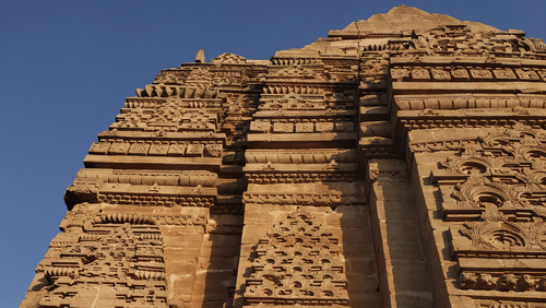 A tall stone facade of a temple within Gwalior Fort, showcasing intricate carvings and detailed architecture.