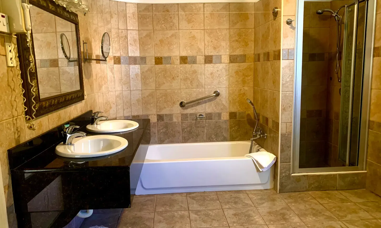 A spacious bathroom with tiled walls and floor includes a bathtub, two sinks with mirrors, and a glass-enclosed shower | Alexander Suite | Altamont Court, Jamaica