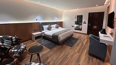 A shot of the deluxe room featuring a bed, bed side tables, two chairs, coffee table, work desk, a couch, a flat screen TV, and a full length mirror - DLS The Emerald, Nainital