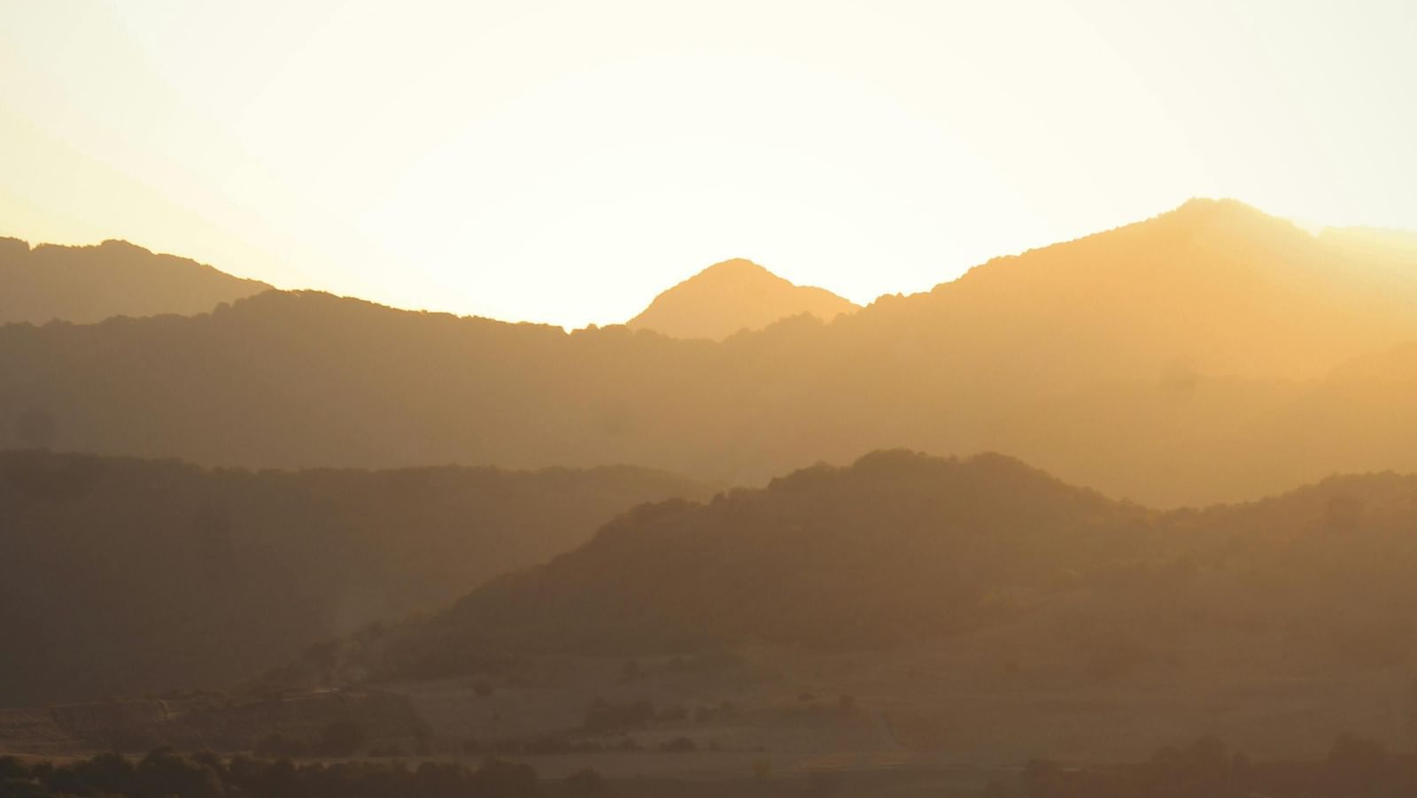 View of rolling mountains shadowed by a bright sun.