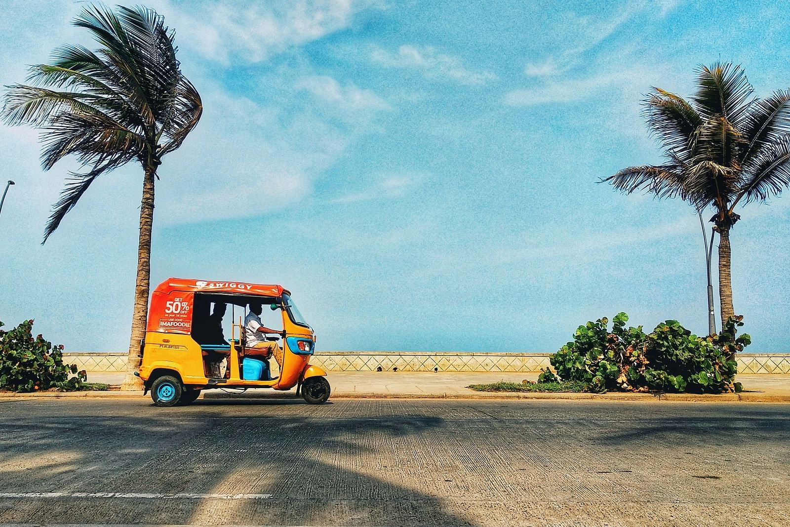 An auto travelling on a road next to the beach with coconut trees.