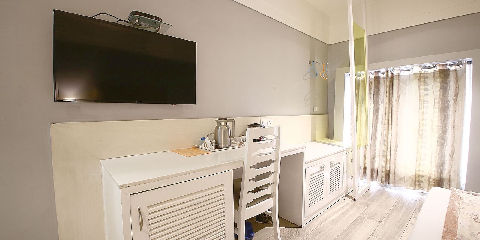 a room with huge windows covered with curtains, table, chairs and a TV 